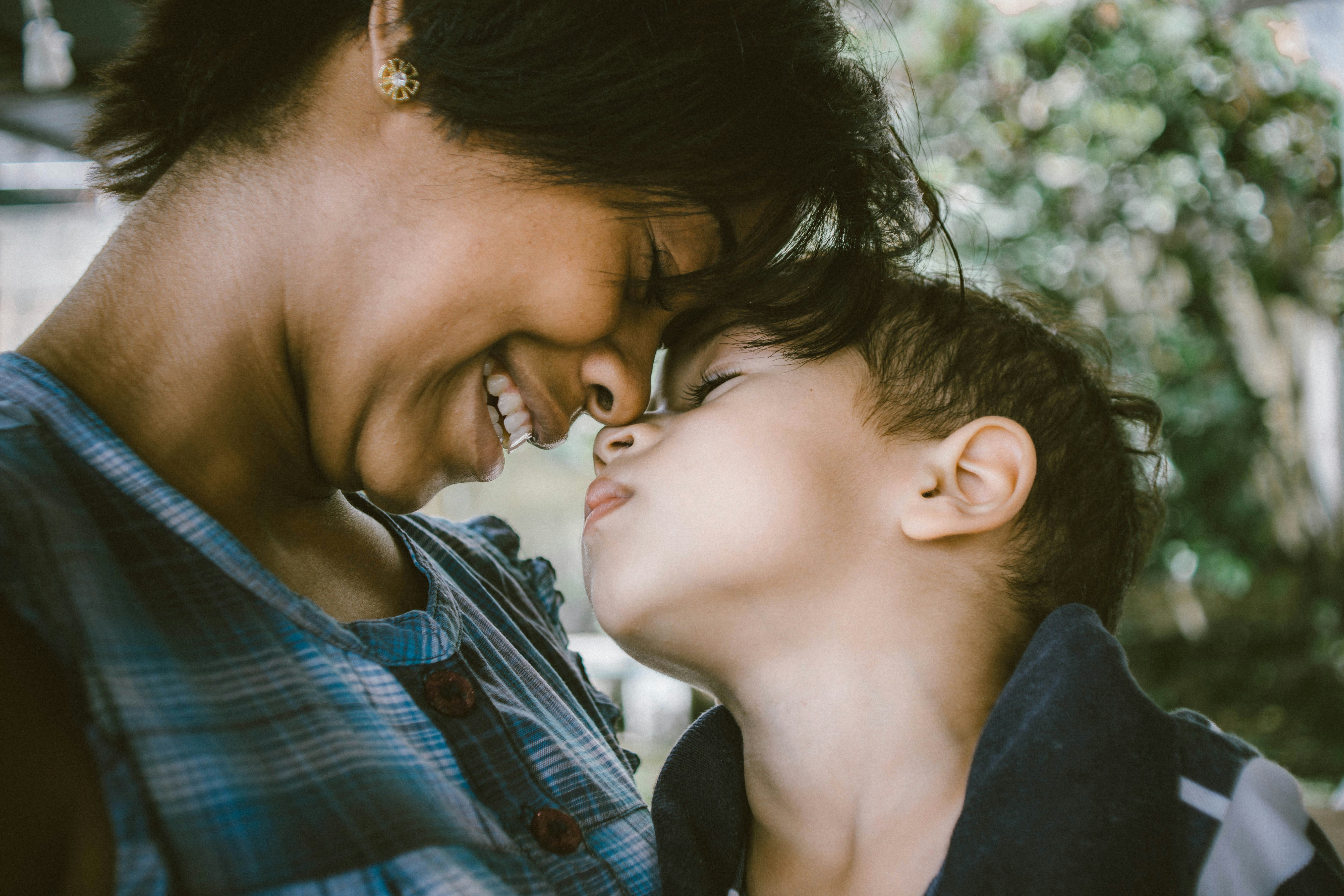 A woman smiles down at her son while she holds him close in her arms while he rests.