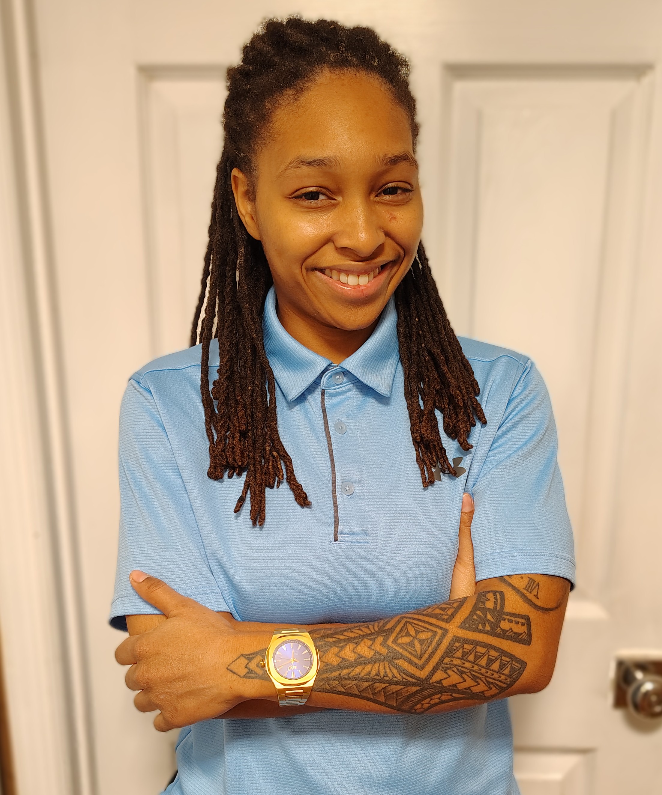 A smiling woman with chest length brown hair, wearing a dark blue shirt, standing with her arms crossed.